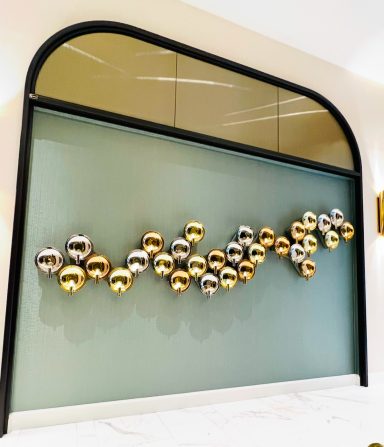 Sculptural wall display with metallic gold and silver spheres arranged in a wave pattern.