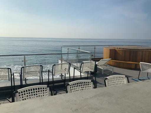 Seaside view with chairs overlooking calm blue water and a distant horizon.