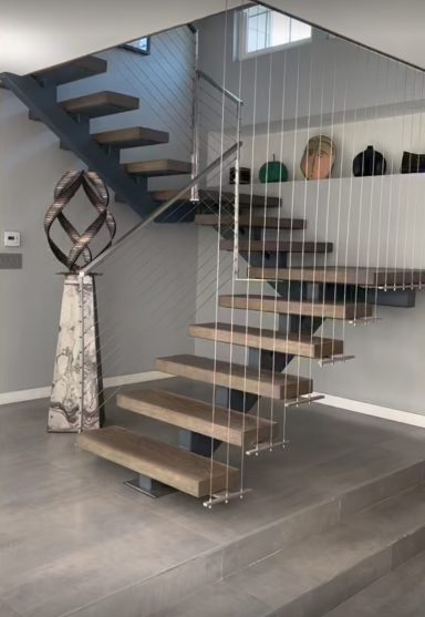 Modern wooden staircase with a glass railing and decorative sculpture nearby.
