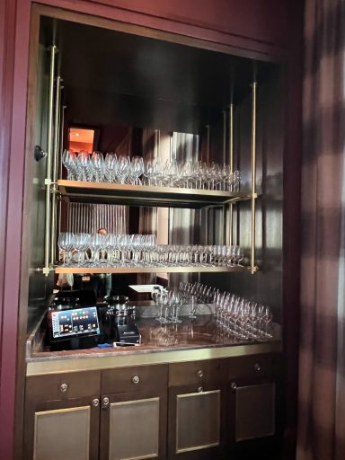 Cabinet with shelves holding various glassware and a tablet on a lower shelf.
