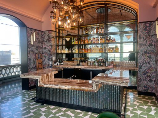 Stylish bar area with marble countertop, shelves of liquor, and modern lighting fixtures.