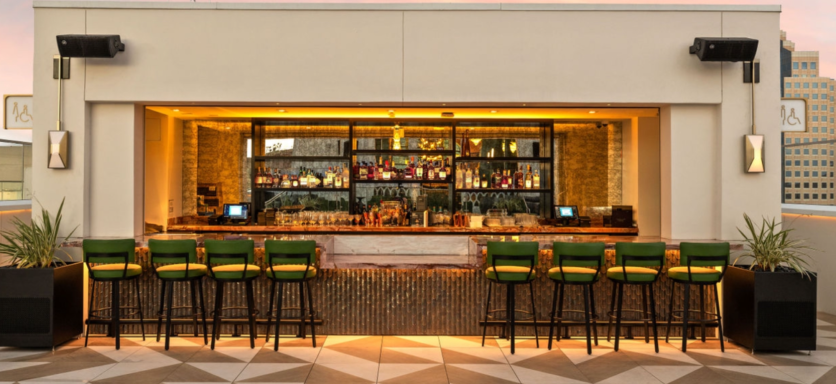 Modern bar area with green stools, warm lighting, and an extensive drink display.