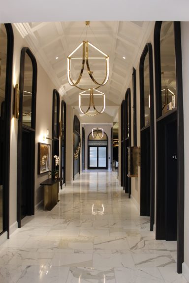 Modern hallway with marble flooring, elegant chandeliers, and dark archway doors.