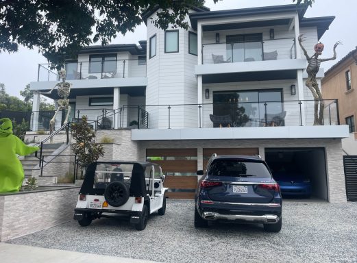 Two modern houses with balconies, a white Jeep, and a dark SUV in the driveway.