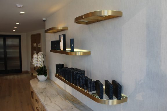 Black products neatly arranged on gold shelves against a light gray wall in a modern setting.