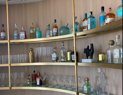 A stylish bar with assorted bottles and glasses on curved shelves.