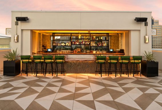 Rooftop bar with illuminated counter and green bar stools against a sunset backdrop.