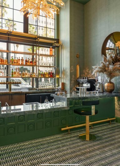 Stylish bar interior with green accents, shelves of bottles, and a decorative chandelier.